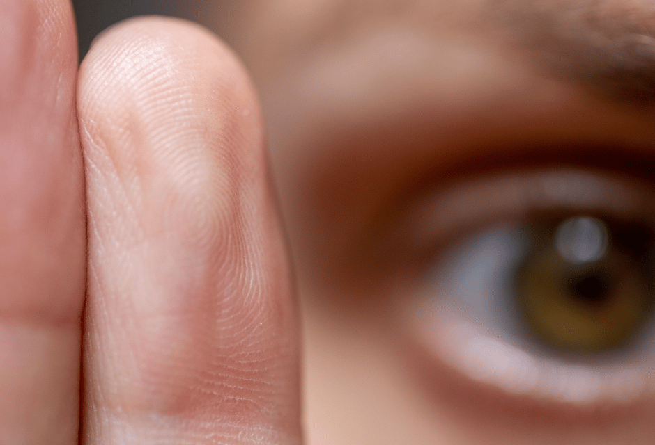 Extreme Nahaufnahme eines menschlichen Auges und dreier Finger mit sichtbarer Hautstruktur und feinen Linien.