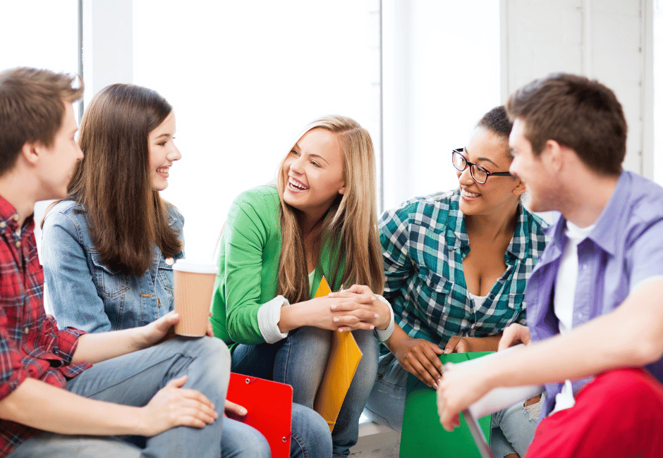 Fünf junge Menschen sitzen in einem hellen Raum zusammen und unterhalten sich freundlich – Szene aus einem Lern- oder Austauschkontext.
