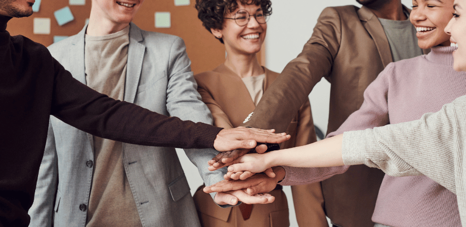 Teammitglieder stehen im Kreis und legen ihre Hände in der Mitte zusammen als Zeichen für Zusammenarbeit und Zusammenhalt im Büro.
